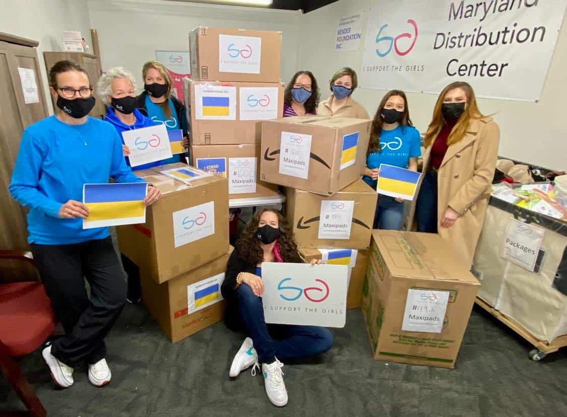 Volunteers standing in front of boxes at the I Support the Girls Maryland warehouse holding Ukranian flags