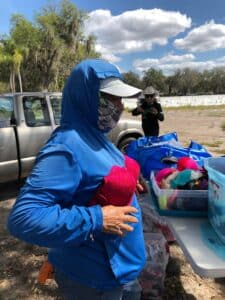 A migrant farm worker trying on a pink bra over their blue hoodie