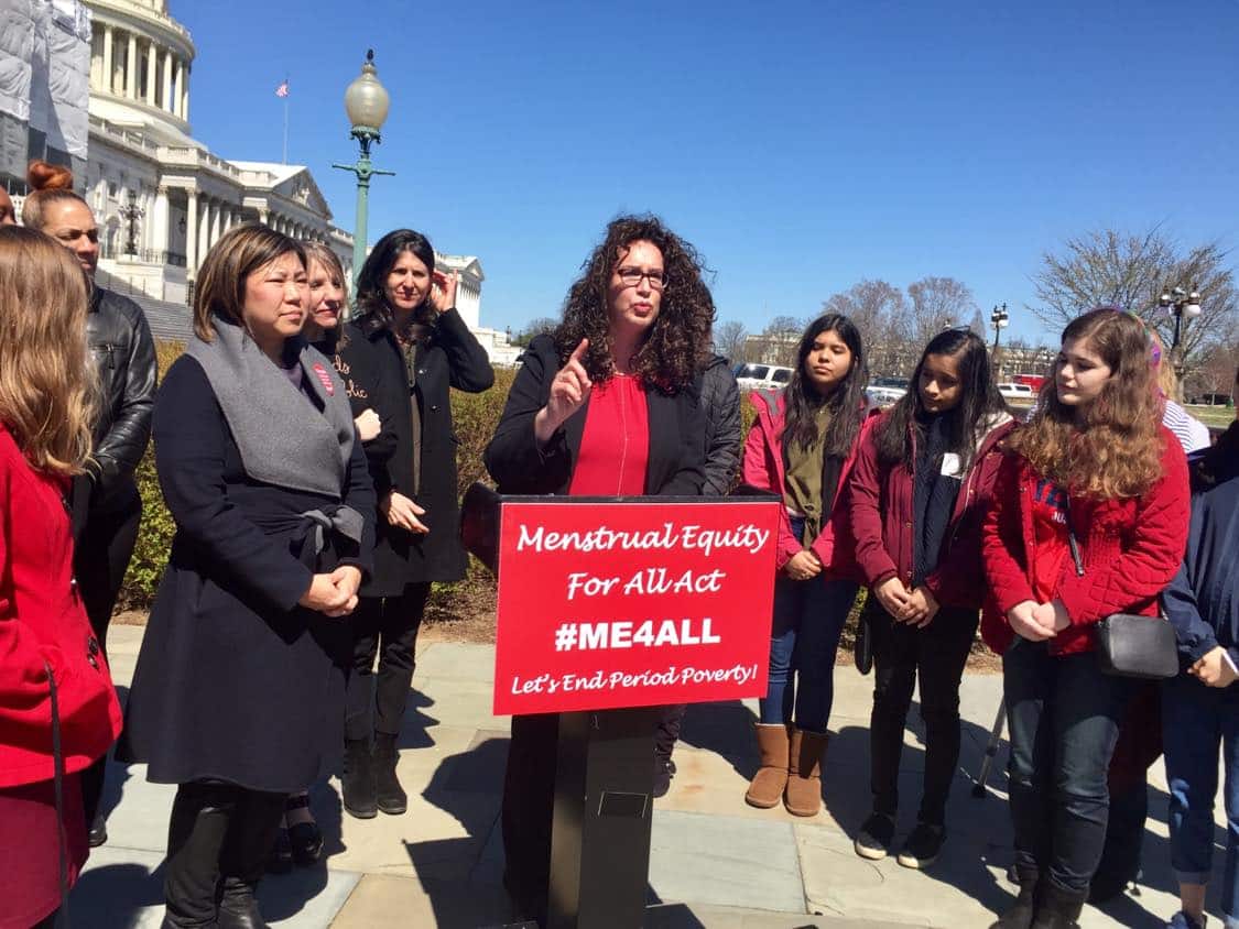 Dana Marlowe speaking in front of the United States Capitol about period poverty and access to menstrual products. To her right is Congresswoman Grace Meng.